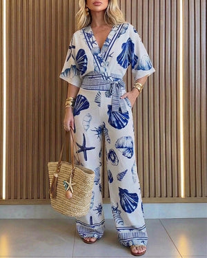 Mono de mujer con estampado oceánico, conchas marinas y estrellas de mar, escote en V cruzado, mangas murciélago, cintura con lazo, perneras anchas y bolsillos